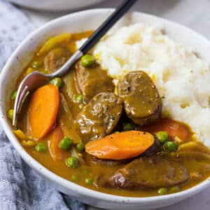 a bowl of curried sausages and mashed potatoes, topped with slices of carrot.