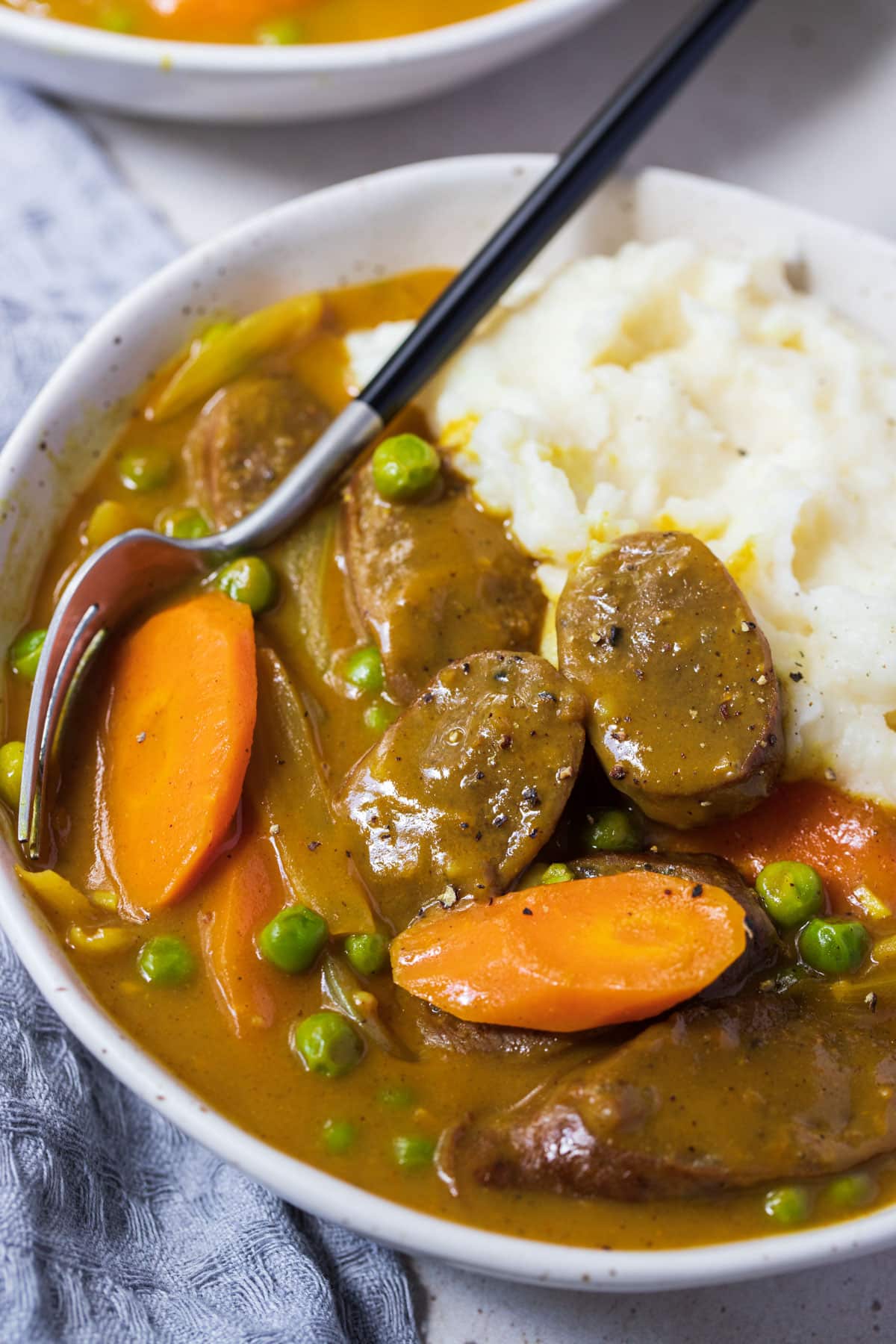 a bowl of curried sausages with mashed potatoes, topped with carrots.