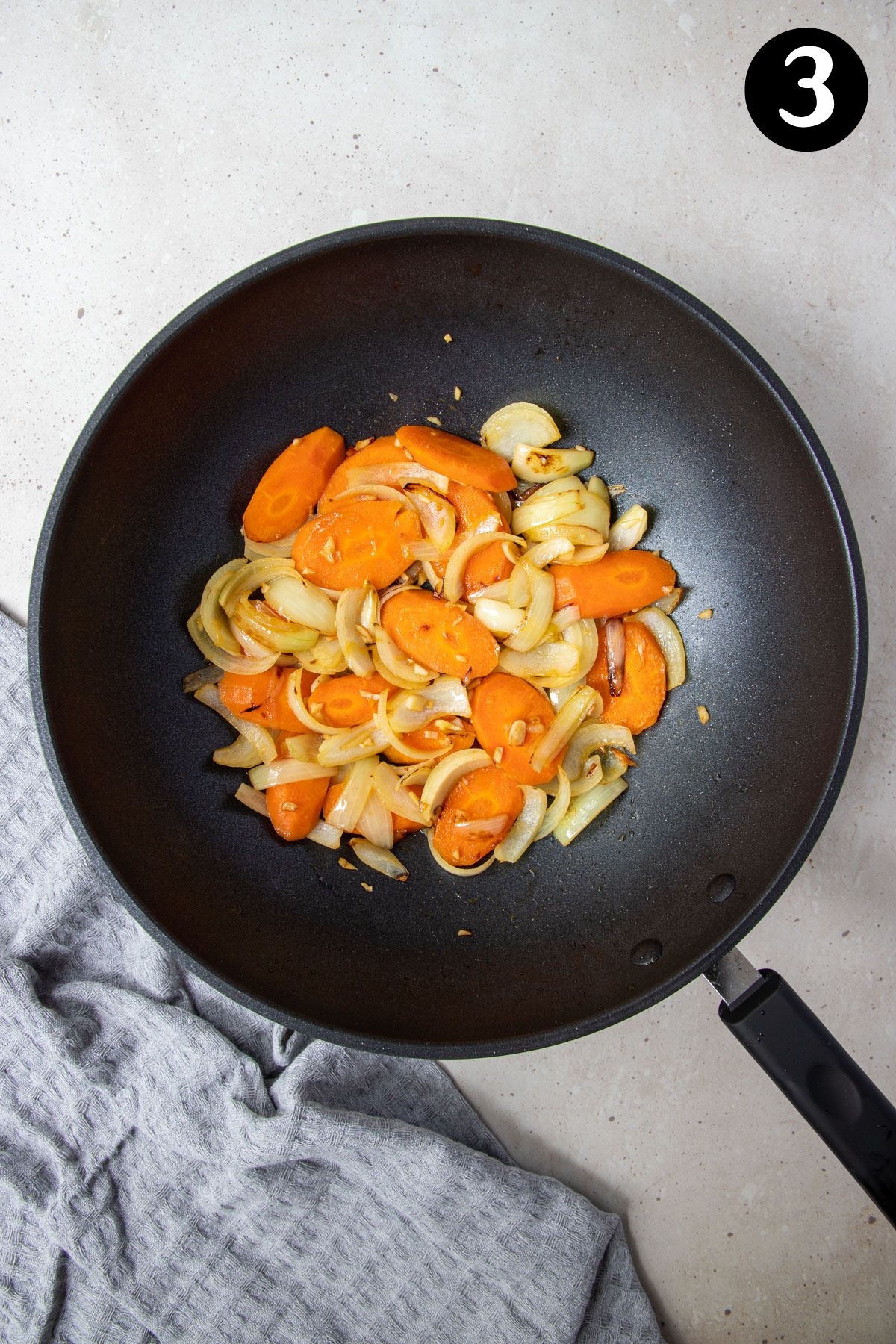 fried onion, garlic and slices of carrot in a frying pan.