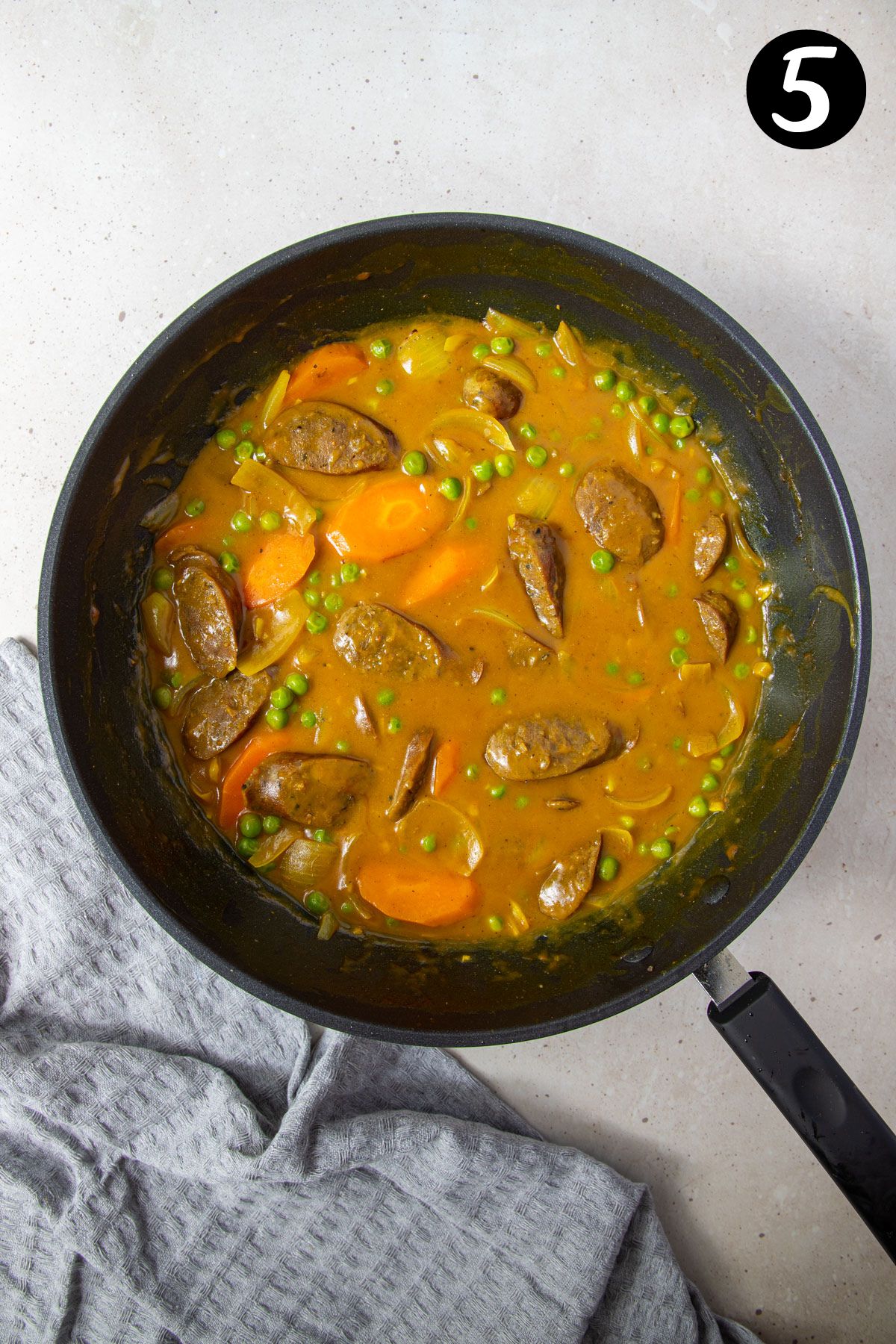 finished curried sausages and vegetables in a thick sauce in a frying pan.