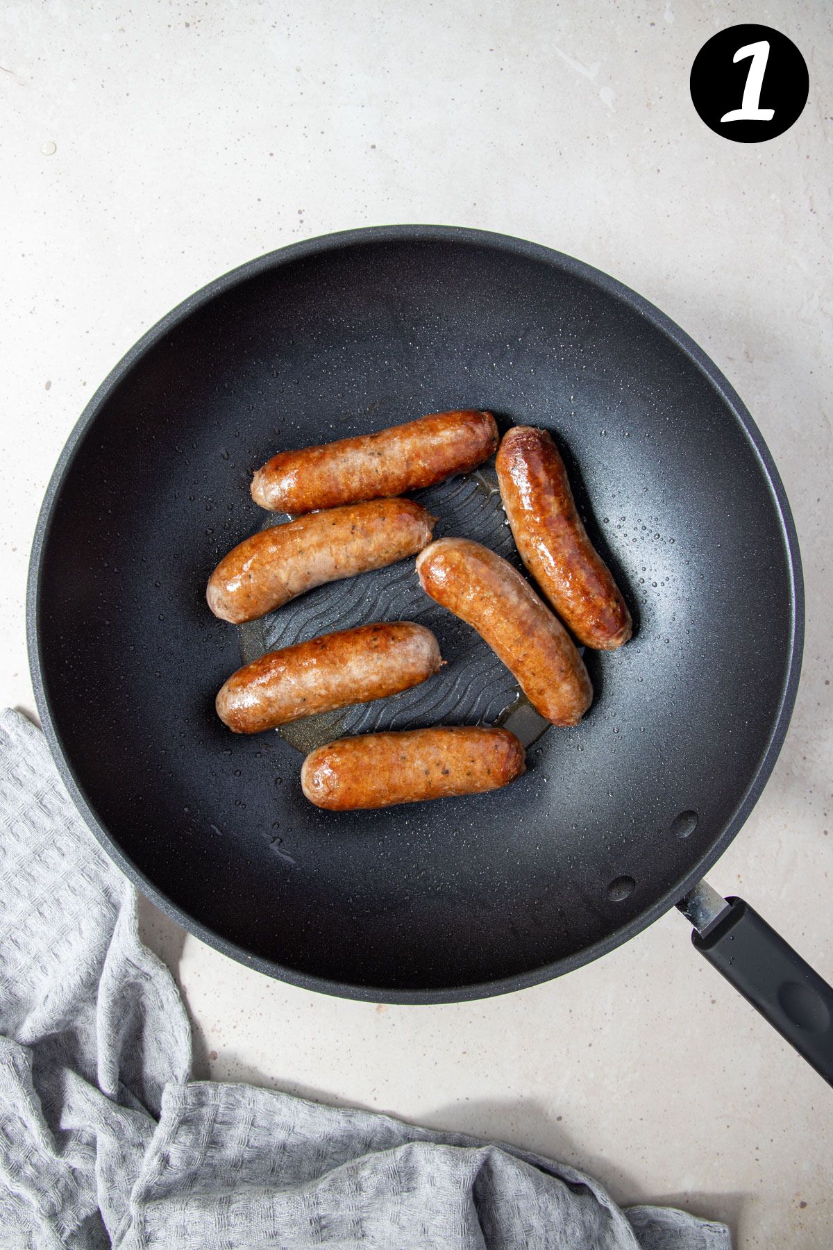 browned sausages in a frying pan.