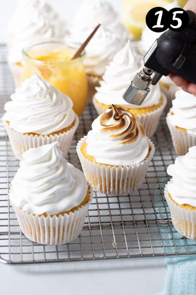 a hand-held blowtorch toasting meringue on top of a cupcake.