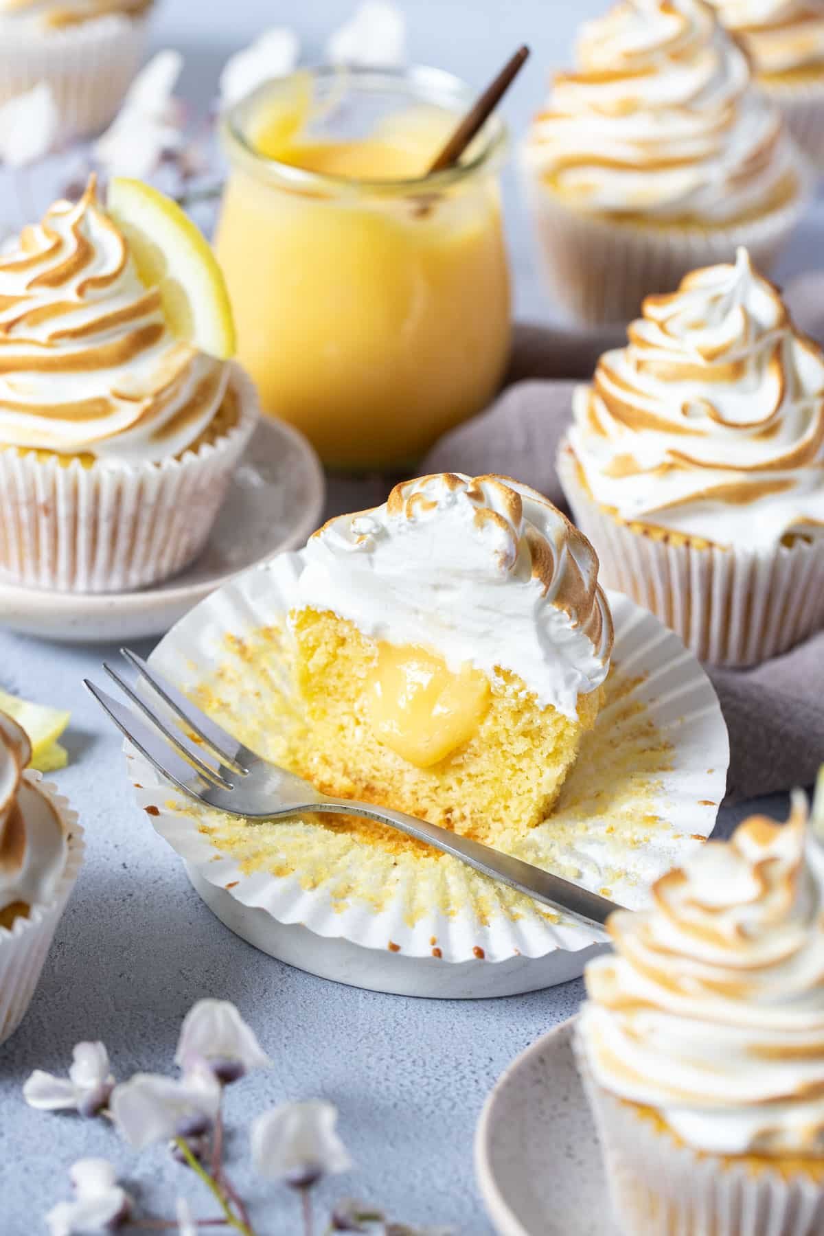 lemon meringue cupcakes on a table. One is cut open showing a lemon curd centre.