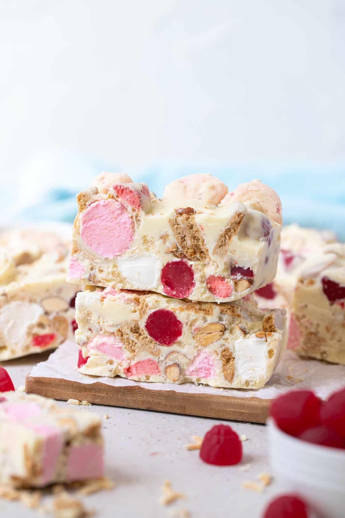 pieces of rocky road on a table with marshmallows and red lollies.