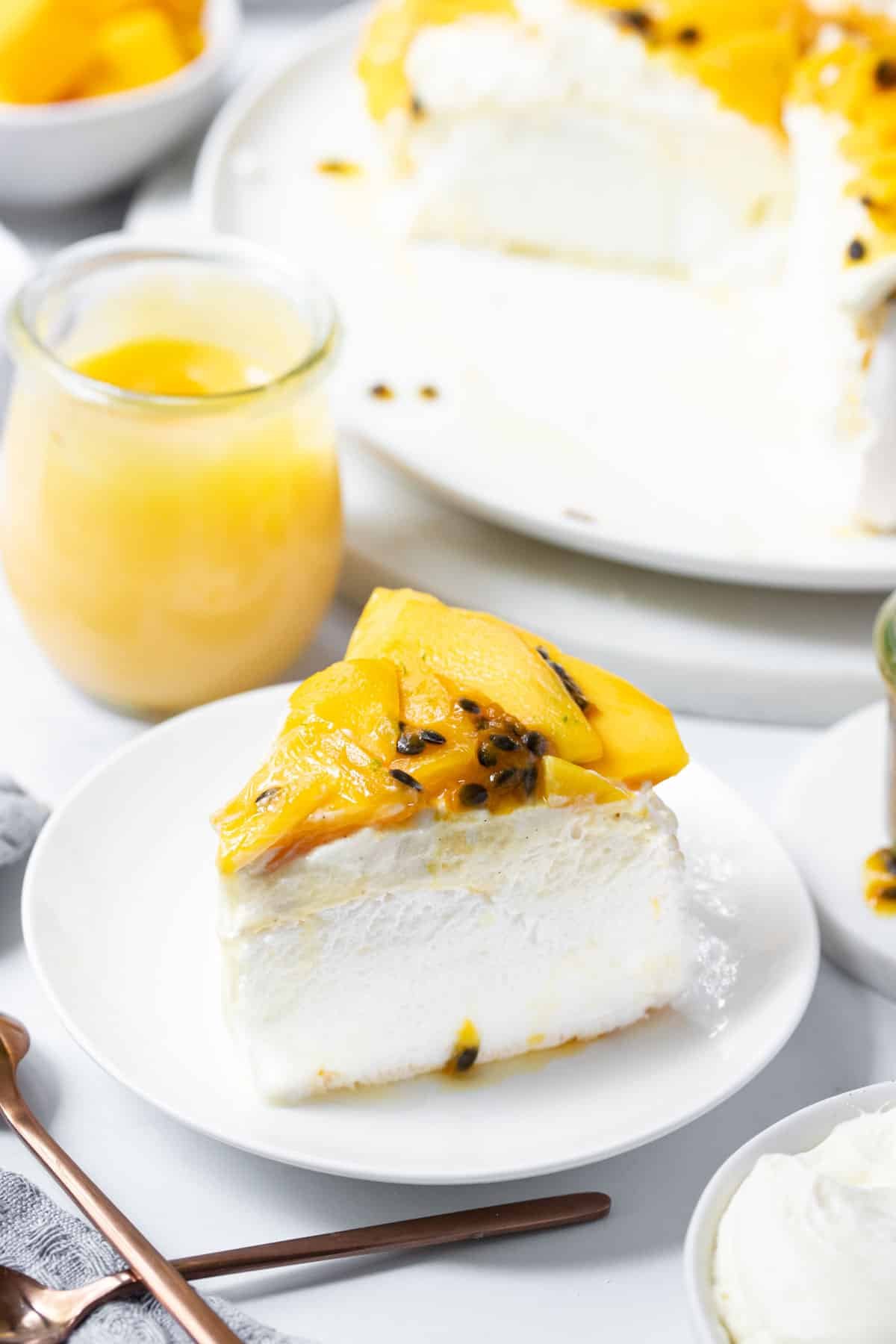 a slice of pavlova on a plate, topped with mango and passion fruit.