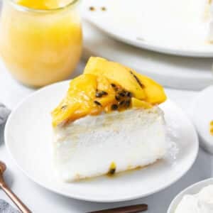 a slice of pavlova on a plate, topped with slices of mango and passion fruit.