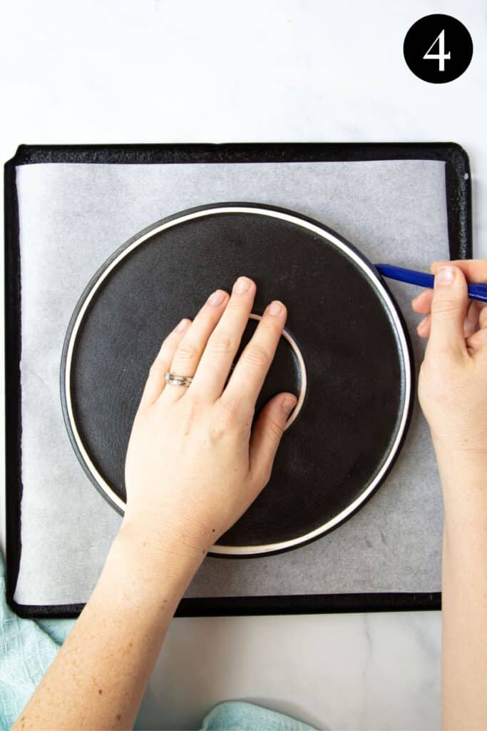 hands tracing a circle on a tray lined with baking paper.