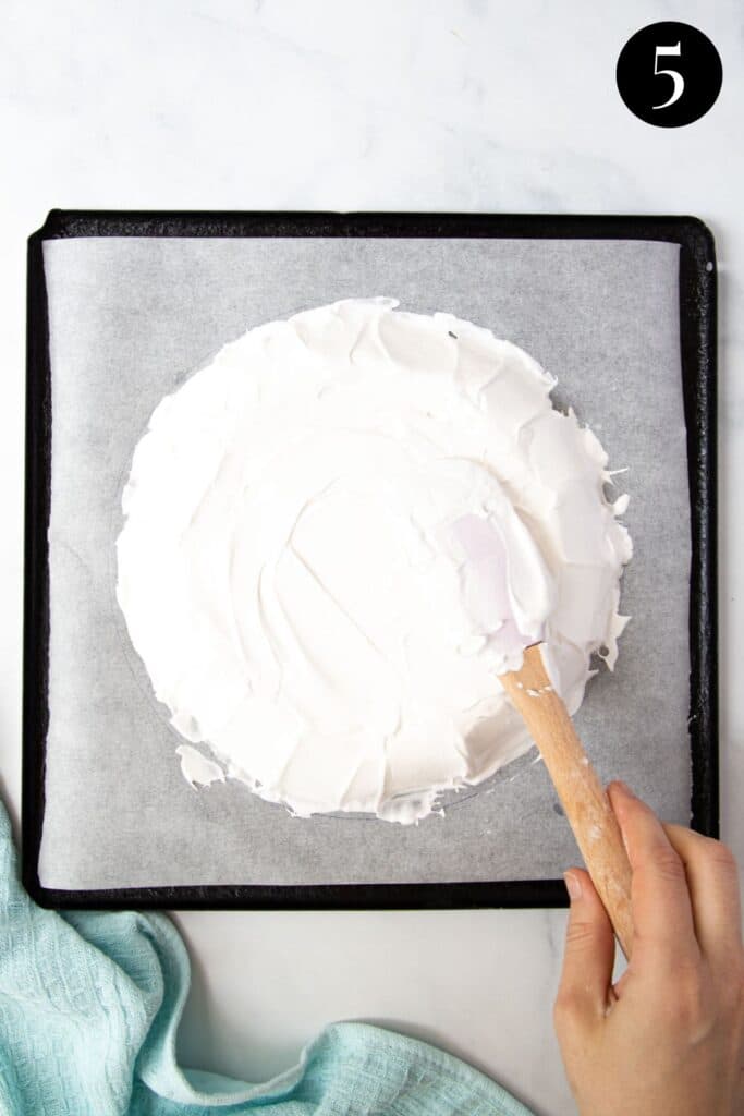 a hand using a spatula to shape meringue on a baking tray.