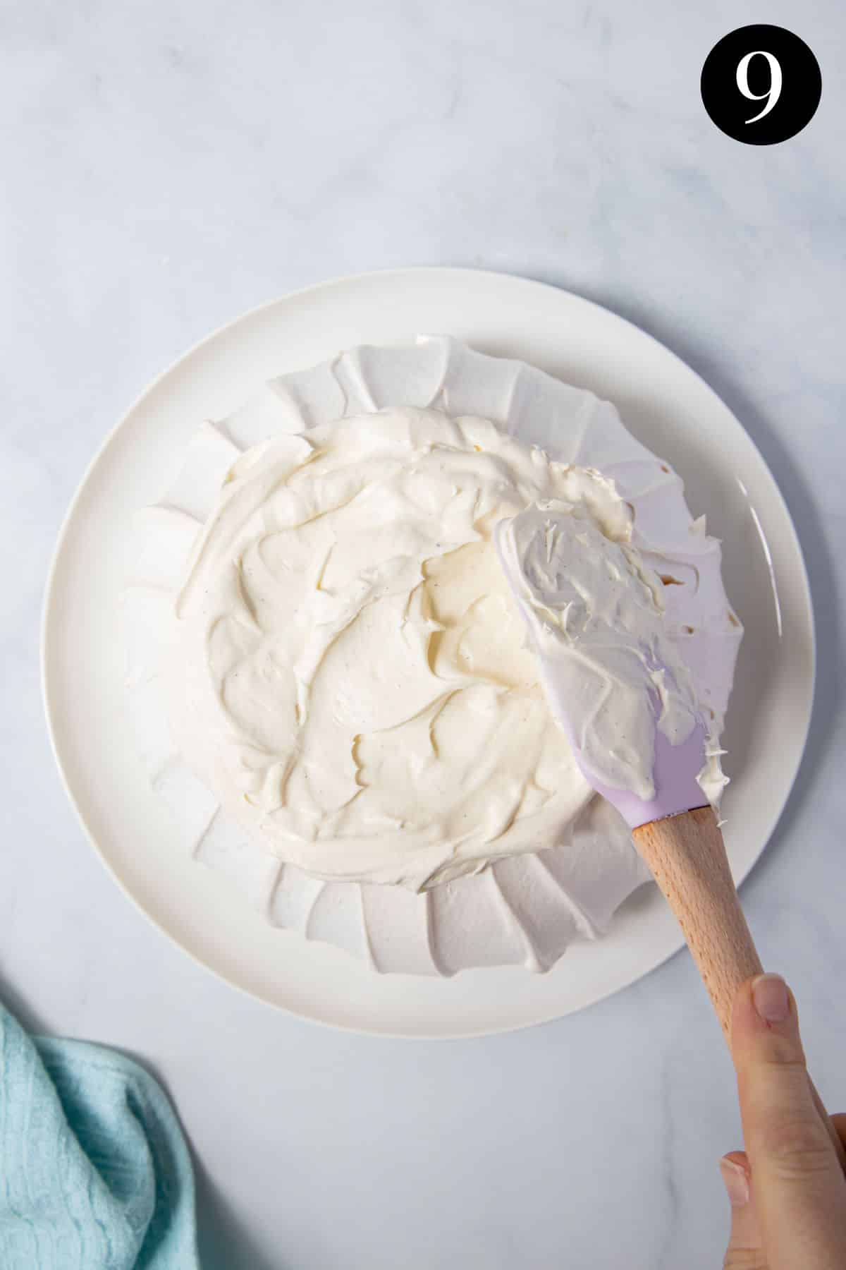 a spatula decorating a pavlova with whipped cream.