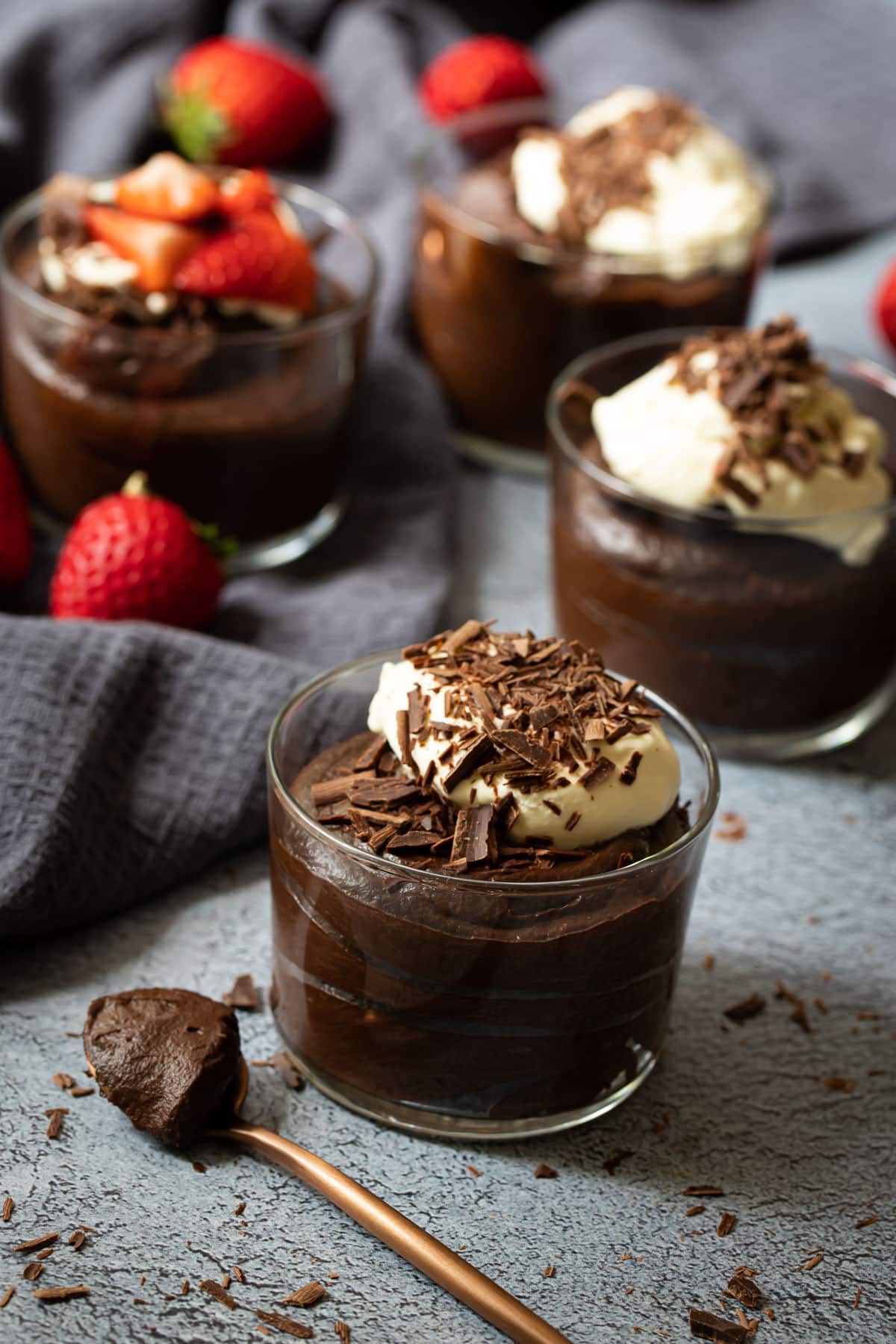 jars of chocolate mousse on a table with strawberries and cream.