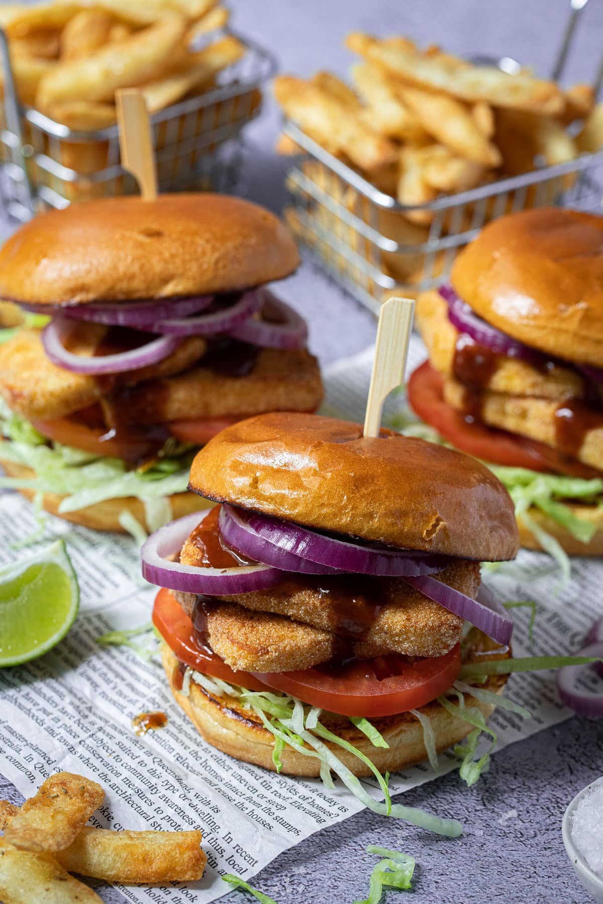 halloumi burgers on a piece of paper with chips and lime wedges.