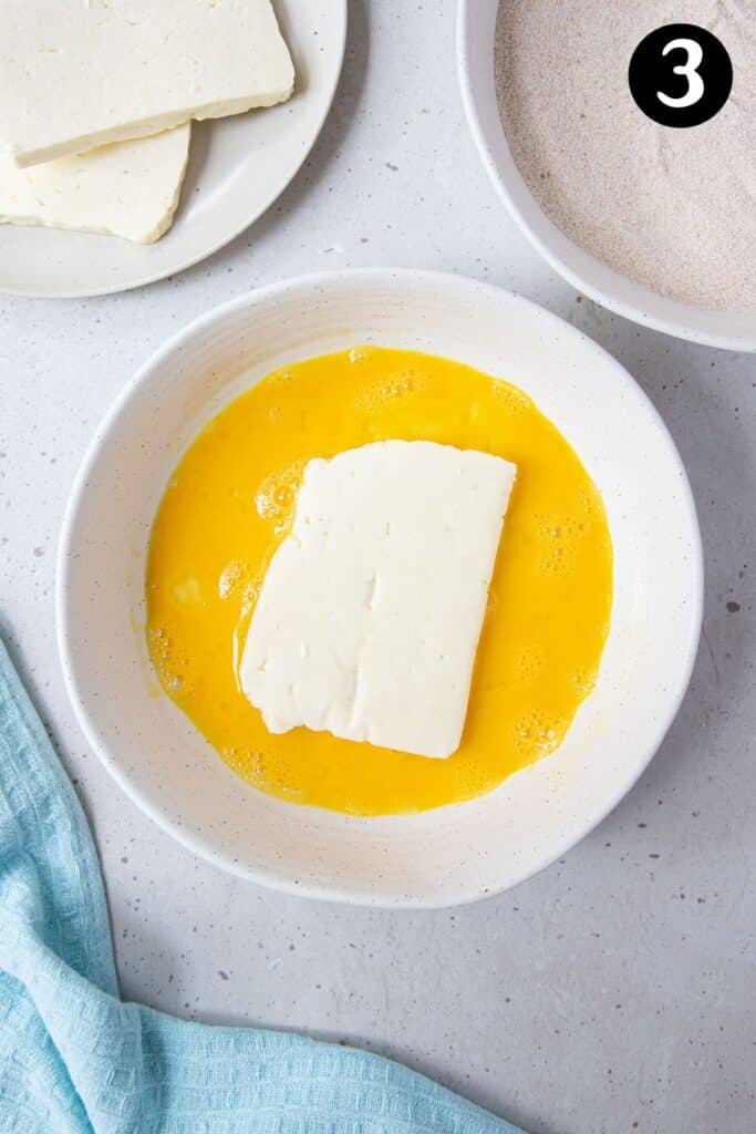 a piece of halloumi in a bowl with beaten egg.