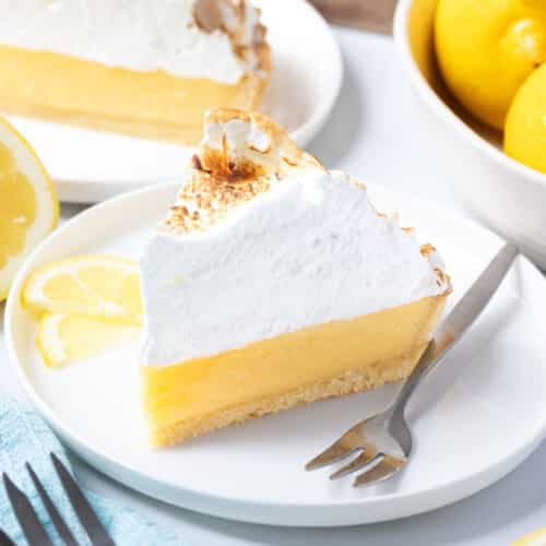 a piece of lemon meringue pie on a plate, with lemon slices and a fork.