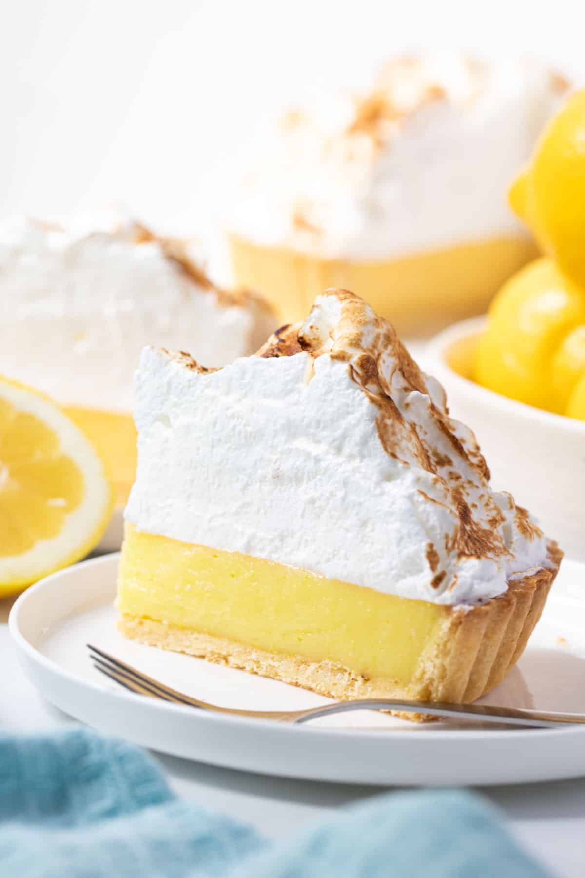 a piece of lemon meringue pie on a white plate, with a fork.