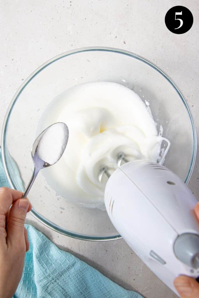 a hand adding sugar to beaten egg whites.