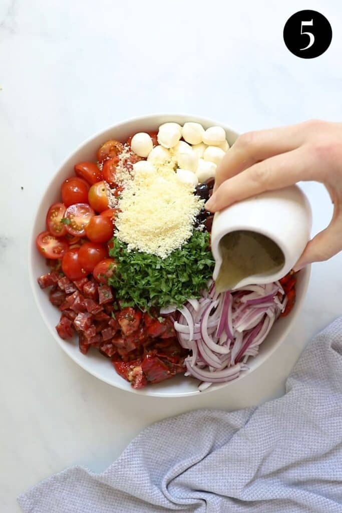 dressing being poured over pasta salad in a bowl.