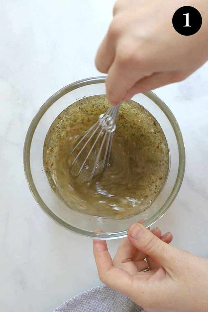 Italian dressing in a bowl. A hand is whisking the dressing.