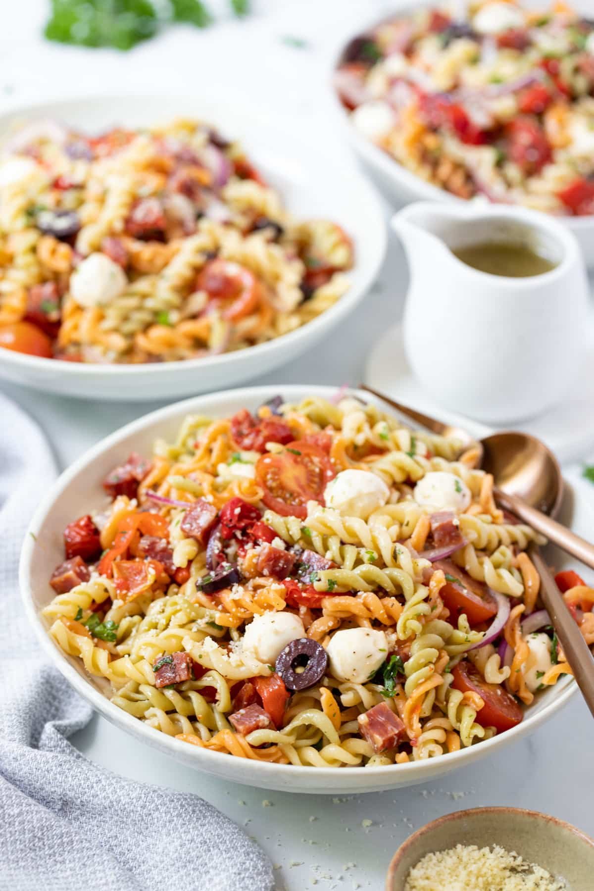 a bowl of pasta salad on a table, topped with salami and vegetables.