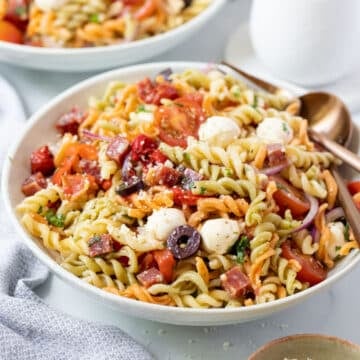 a bowl of salami pasta salad topped with herbs and bocconcini.