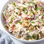 a bowl with potato salad with bacon, onion and egg, topped with dill and chives.