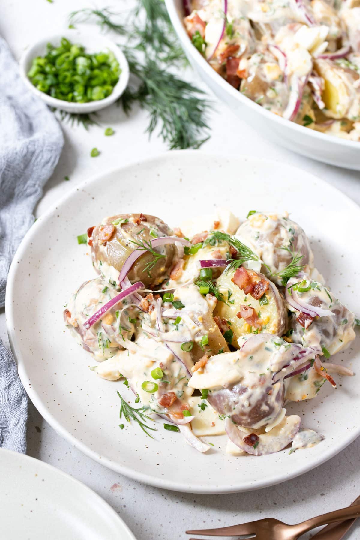 potato salad on a plate, topped with pieces of bacon and dill.