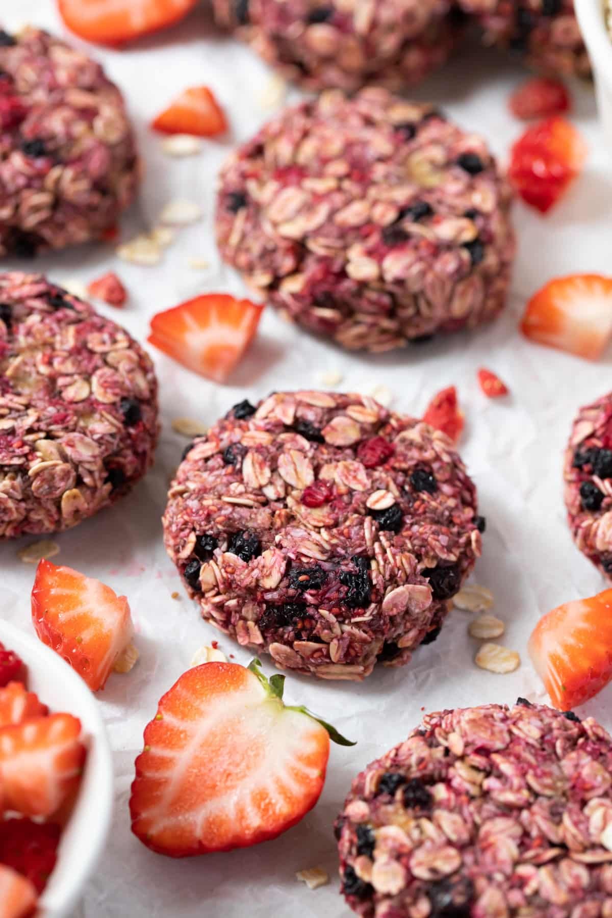 cookies on a table with slices of strawberries and crushed raspberries.