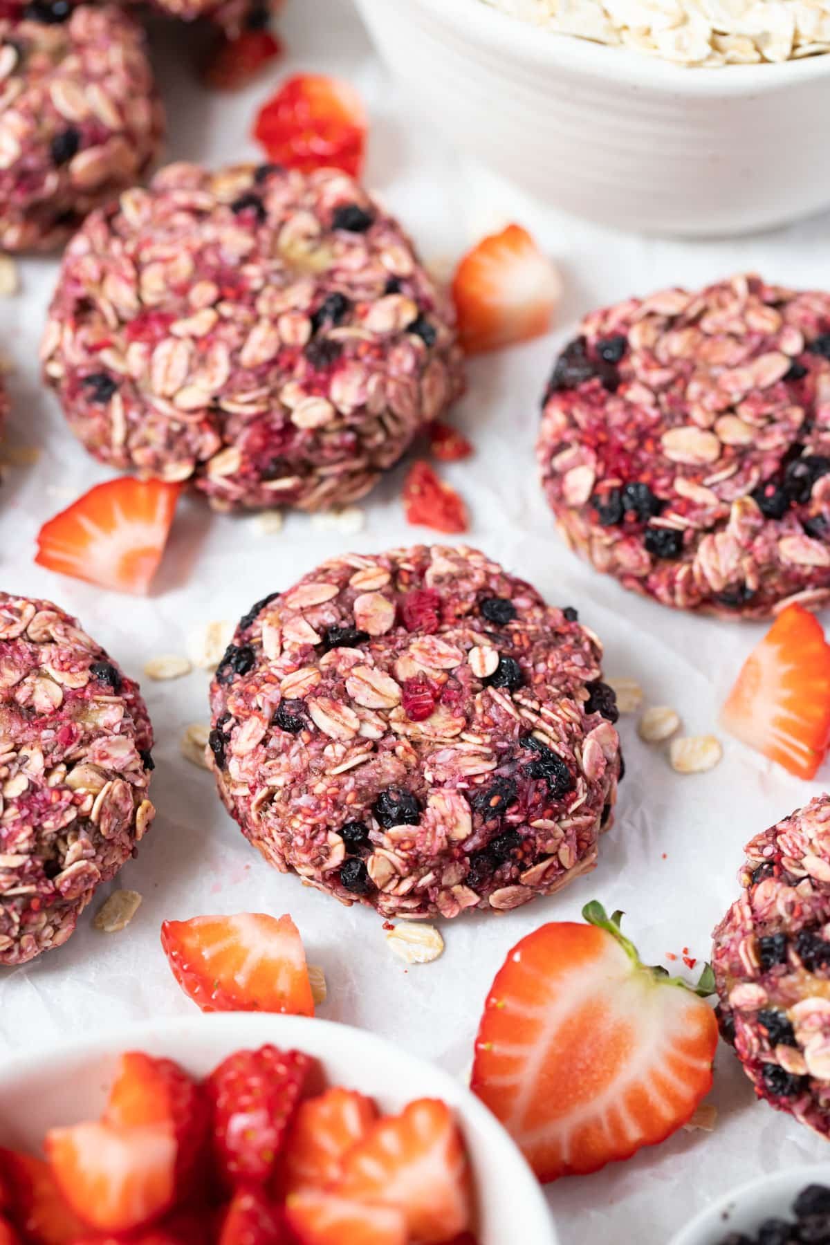 raspberry cookies on a table with slices of strawberries.