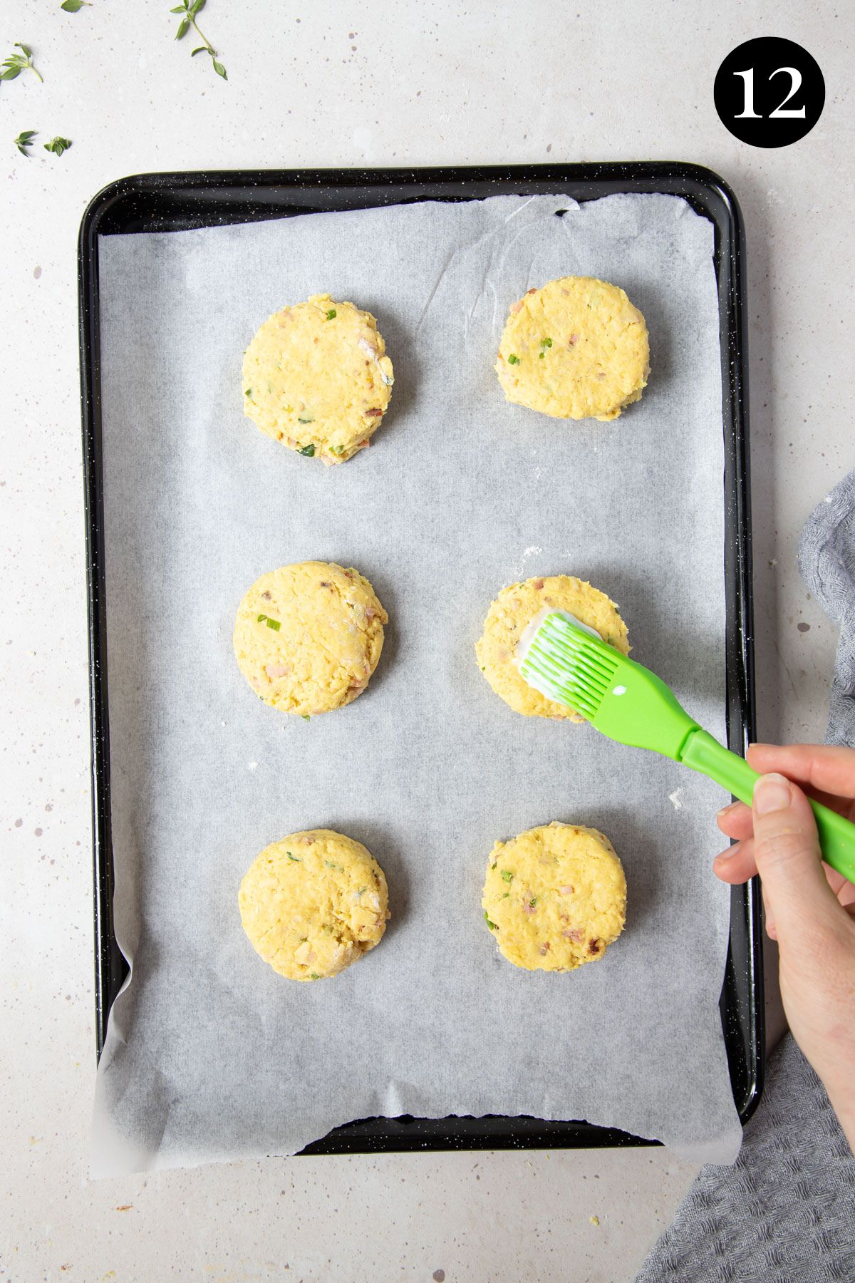 a hand brushing buttermilk over the top of scones, on a baking tray.