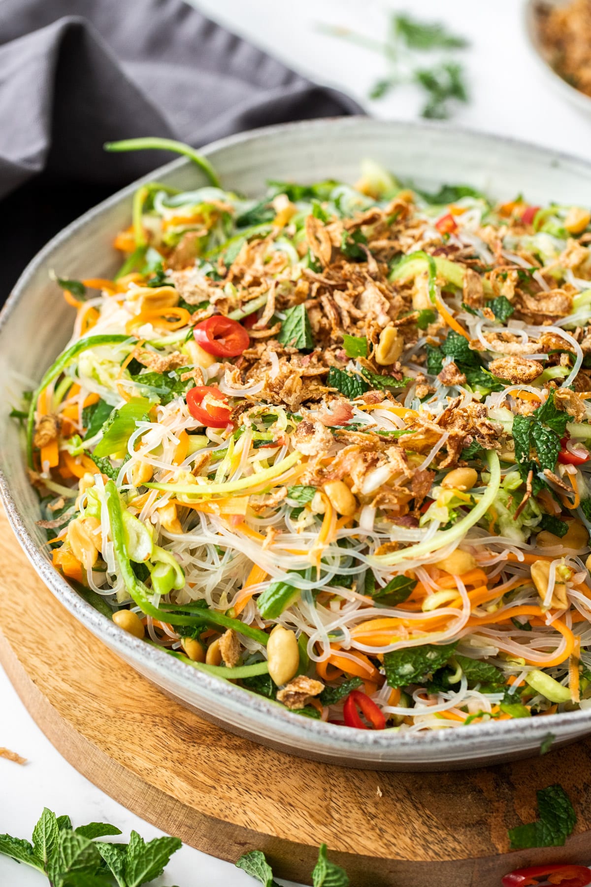 a bowl of vermicelli noodle salad topped with chopped vegetables, mint and shallots.