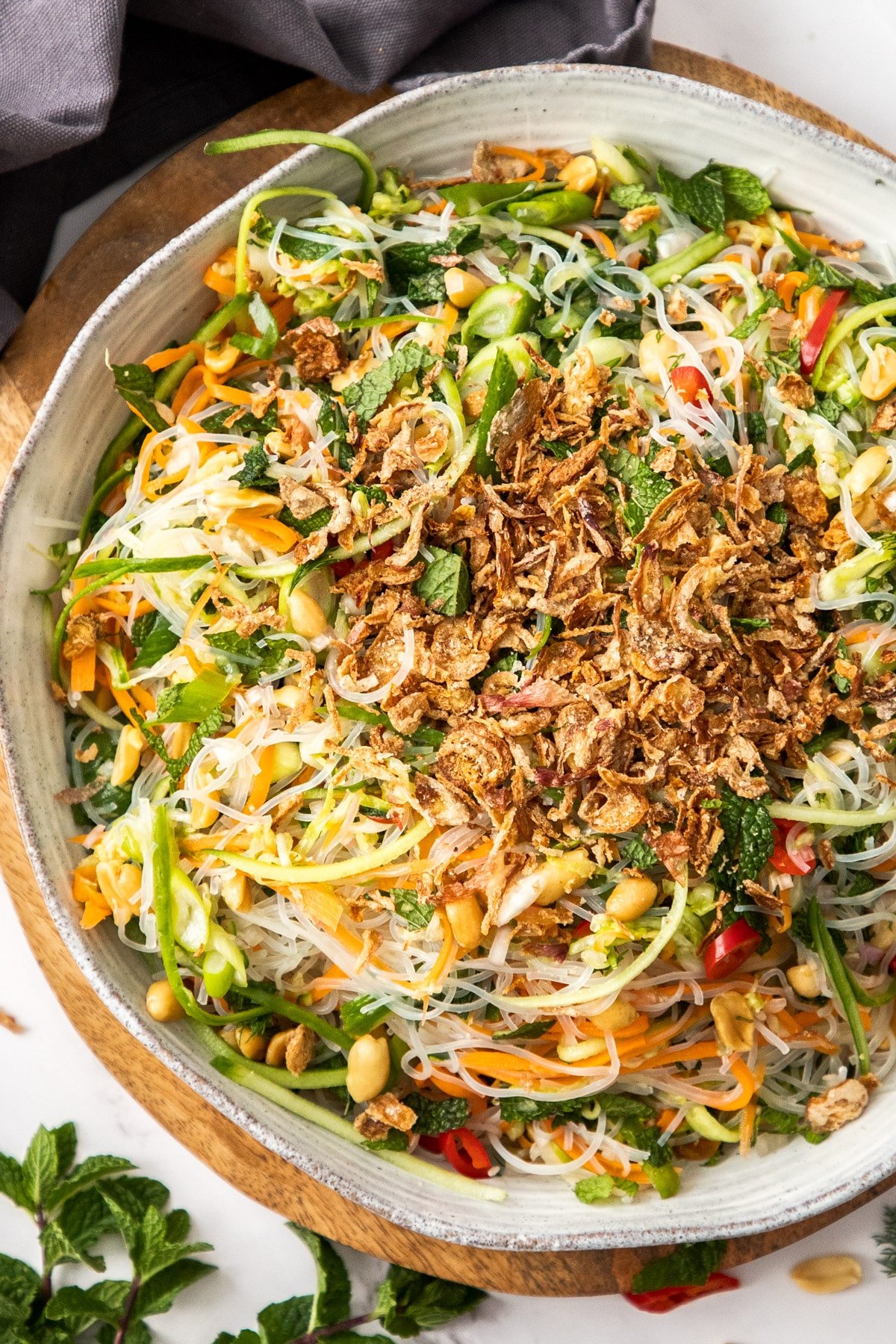 a bowl of vermicelli noodle salad topped with chopped vegetables and shallots.