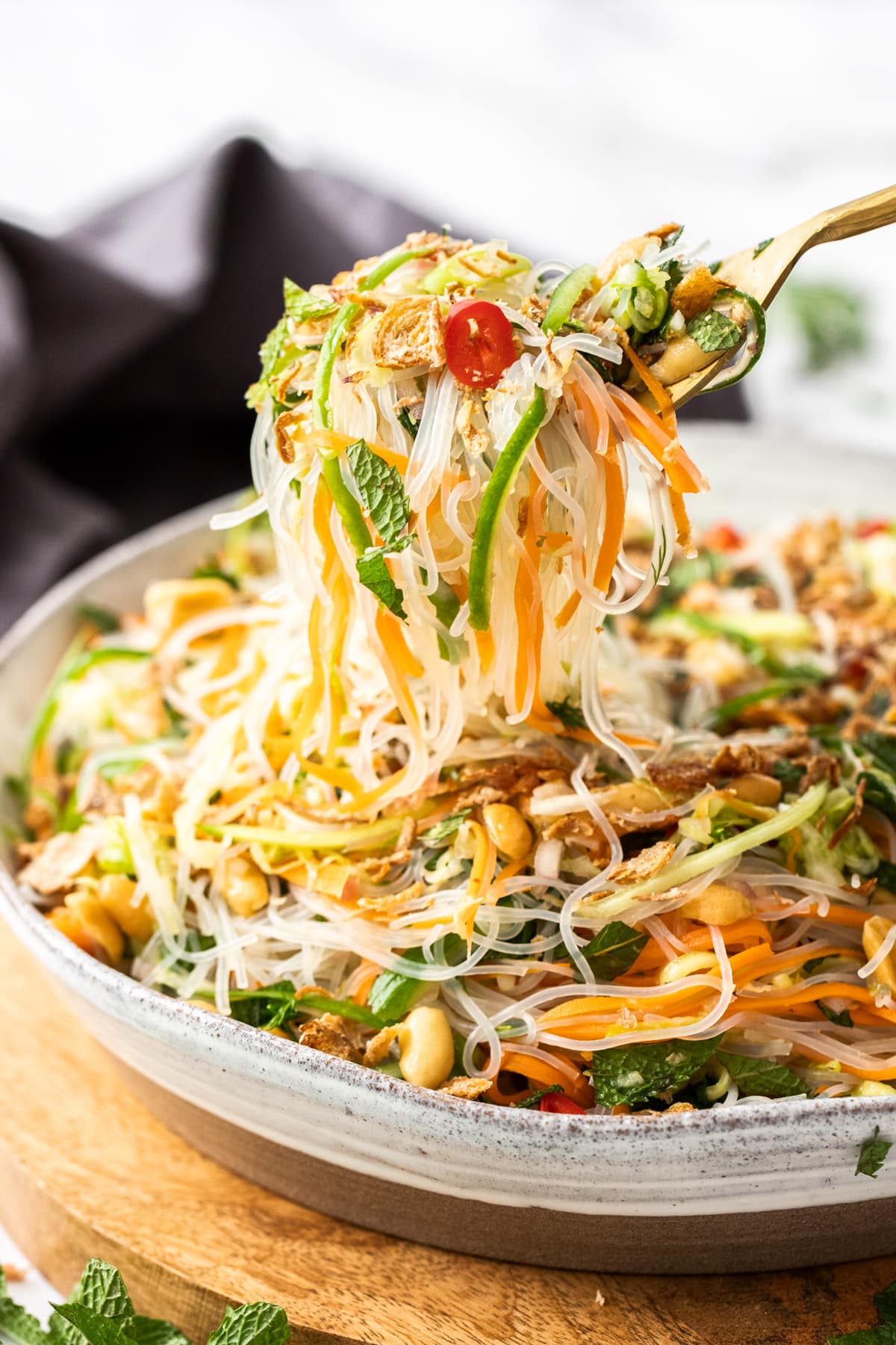 a fork holding vermicelli noodles and salad, over a bowl.