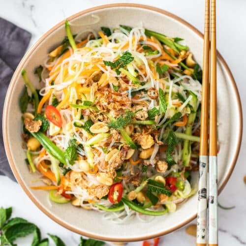 a bowl of salad with vermicelli rice noodles, vegetables and mint.