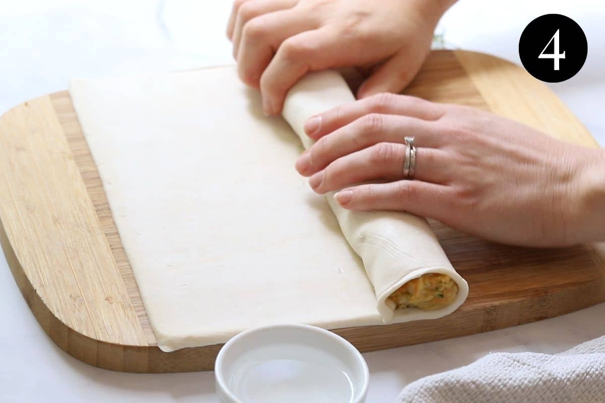 hands rolling puff pastry over chicken mince filling.