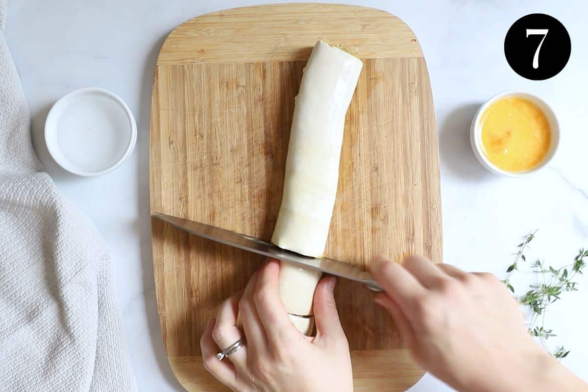 hands using a knife to cut through a sausage roll on a wooden board.