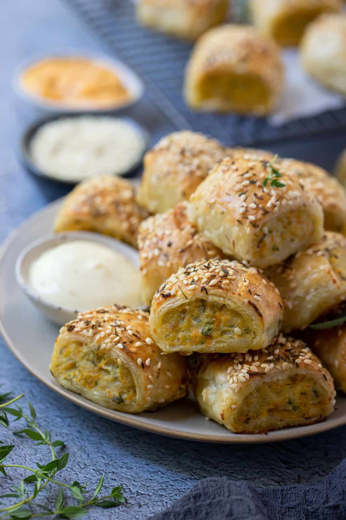sausage rolls piled on a plate, with dipping sauce.