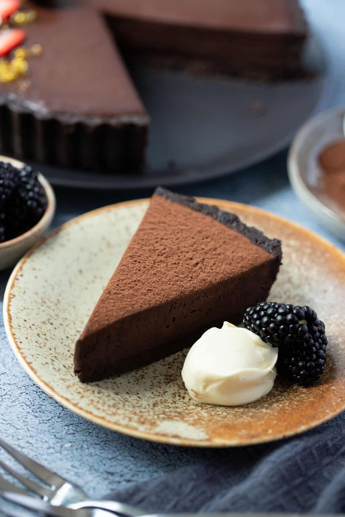 a slice of chocolate tart on a plate with a dollop of cream and fresh blackberries.