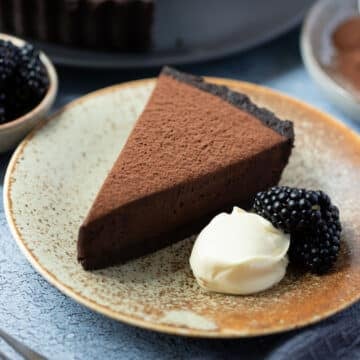 a slice of chocolate tart on a plate with cream and blackberries.