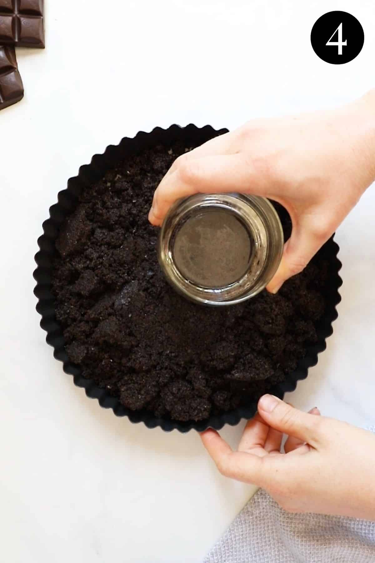 a hand using the bottom of a cup to press biscuit mixture into a tart tin.