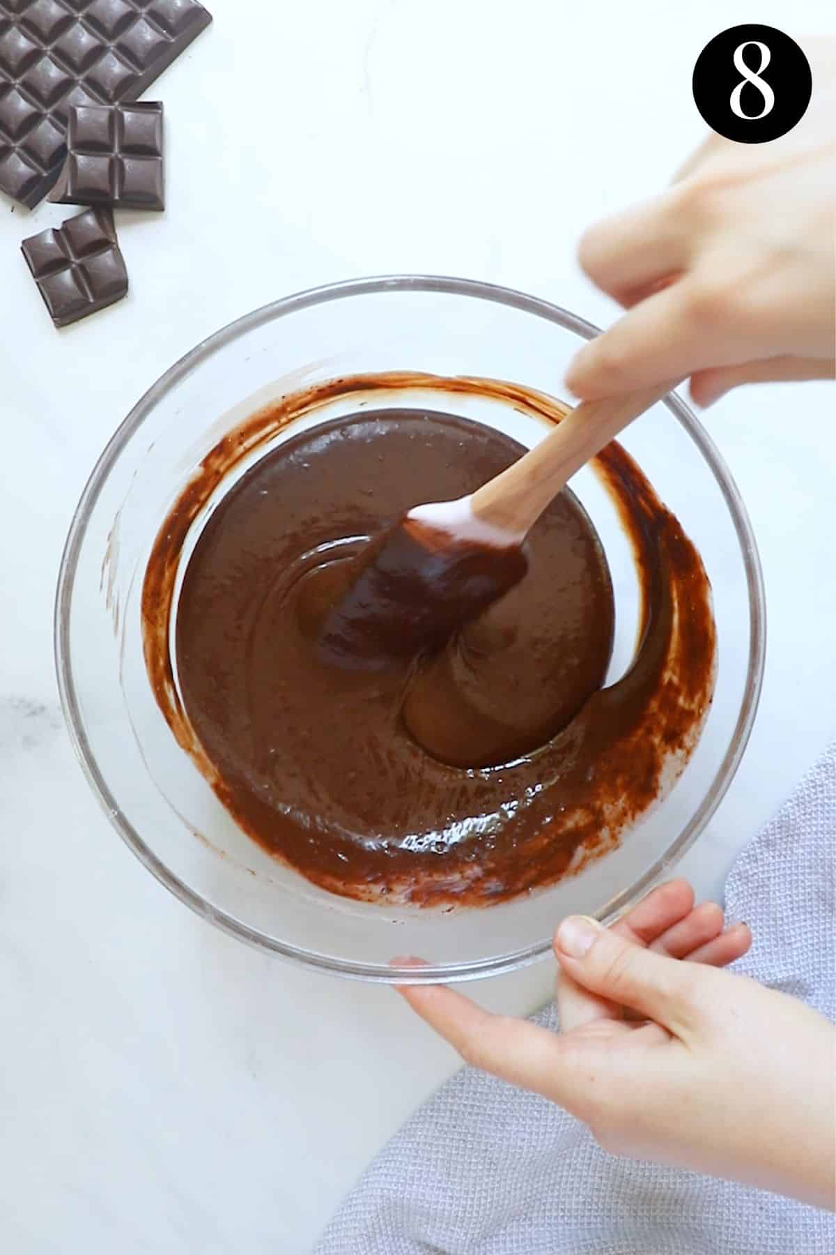 hands stirring chocolate ganache in a glass bowl.