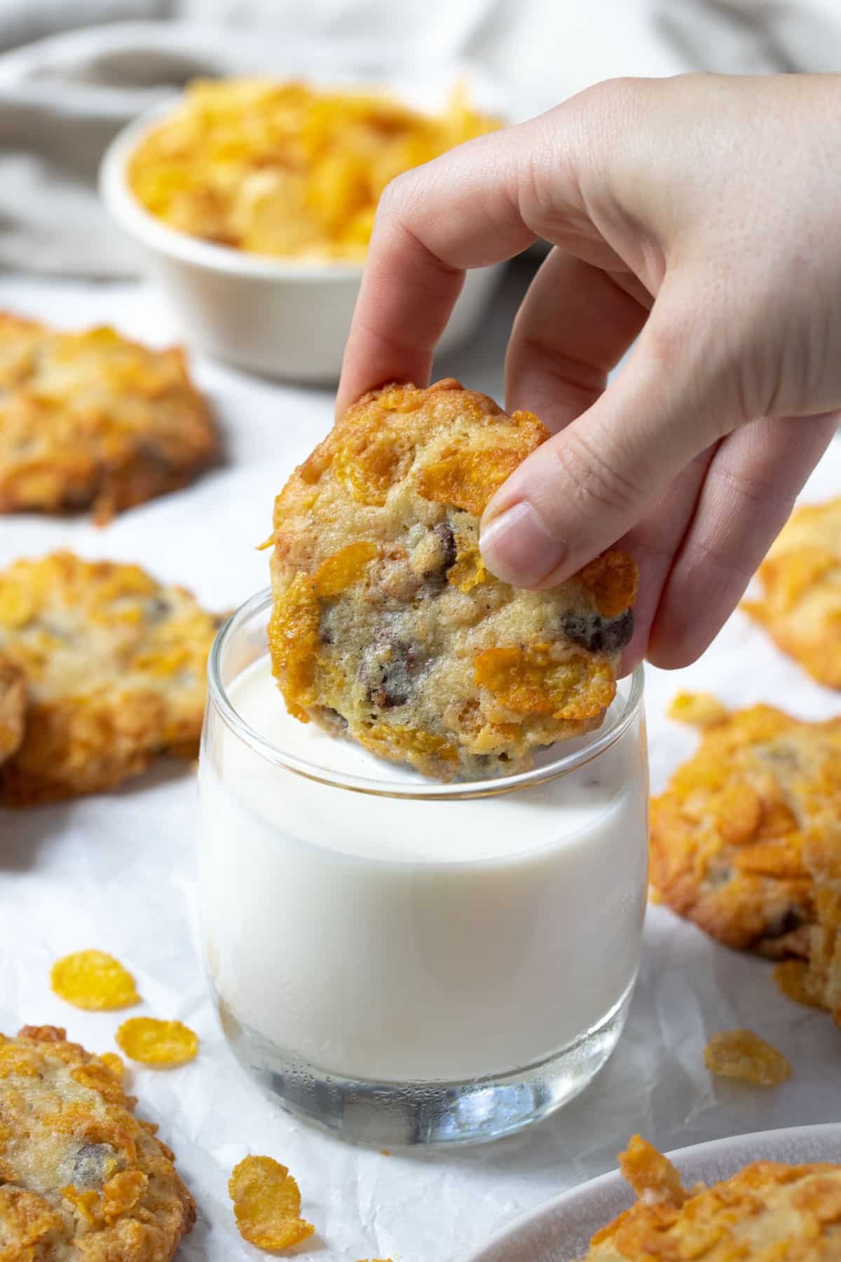 a hand dipping a cookie into a glass of milk.