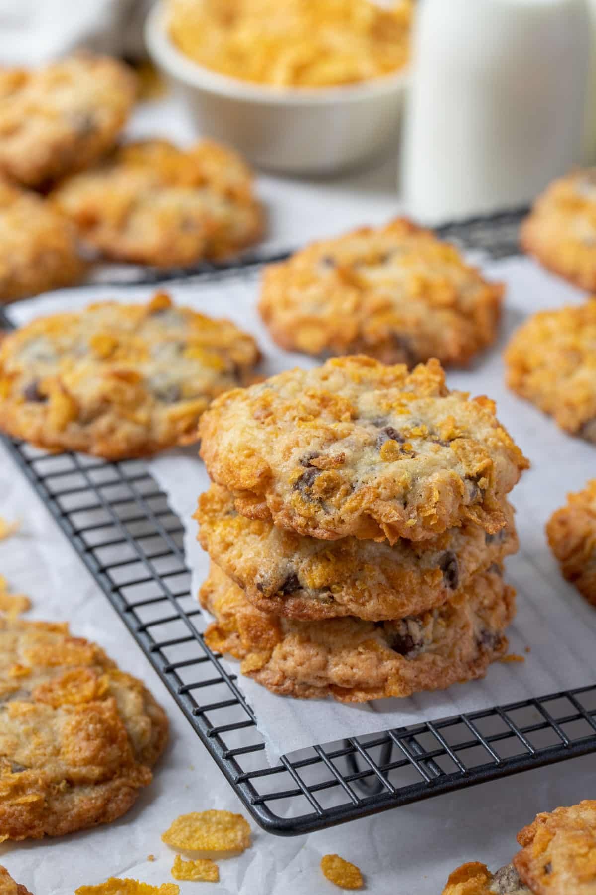 cookies stacked on a wire rack, with corn flakes and bottles of milk.