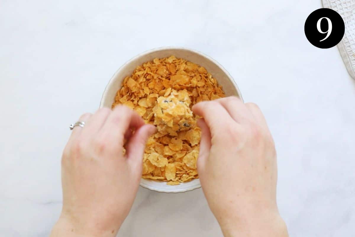 hands rolling a ball of cookie dough in corn flakes.