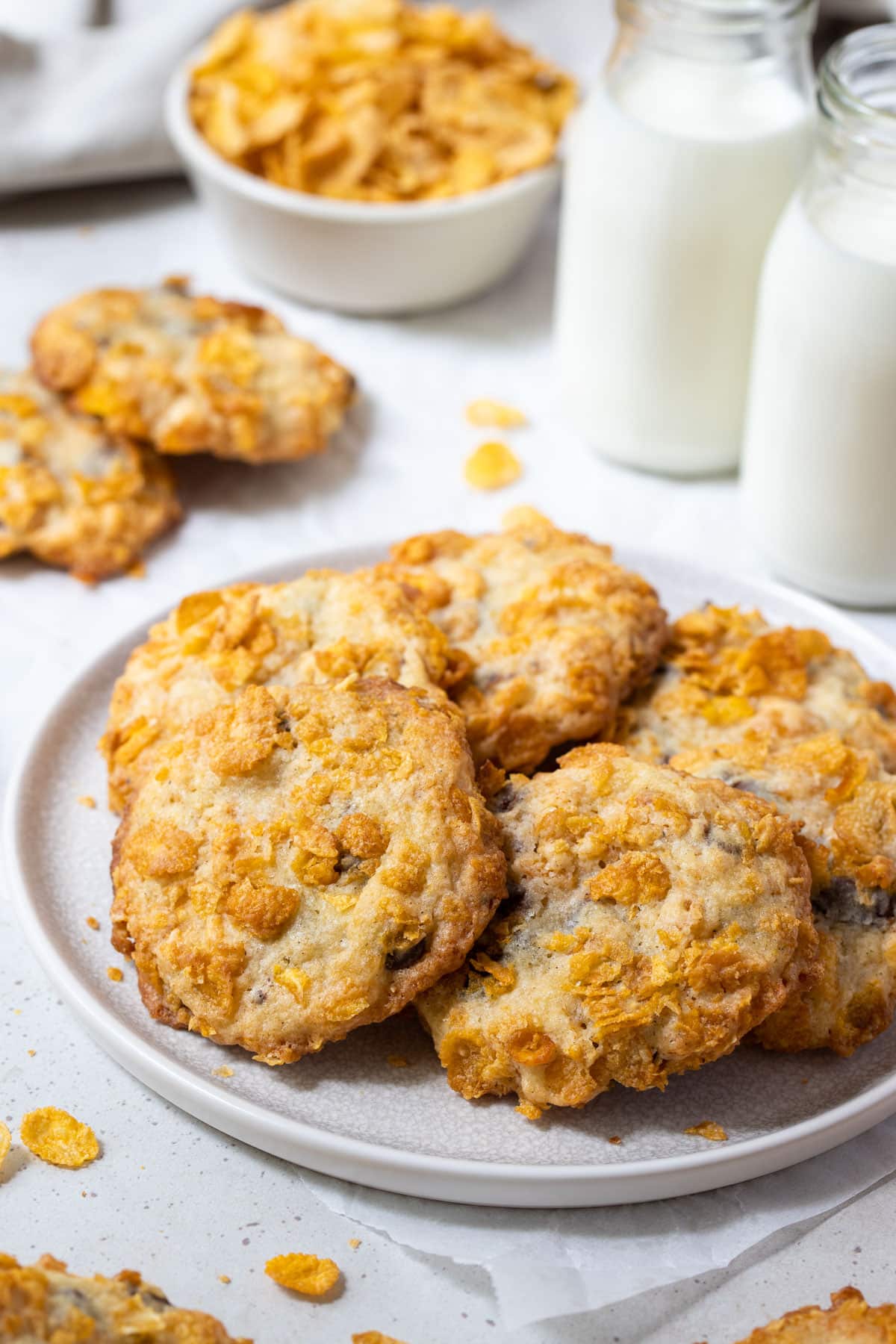 a plate of cookies, coated in cornflakes with bottles of milk.