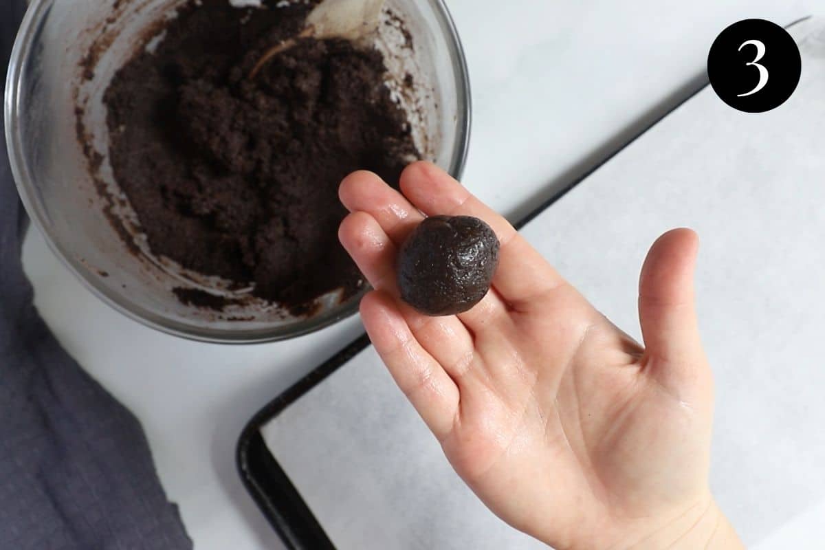 a hand holding Oreo mixture that has been rolled into a ball. 