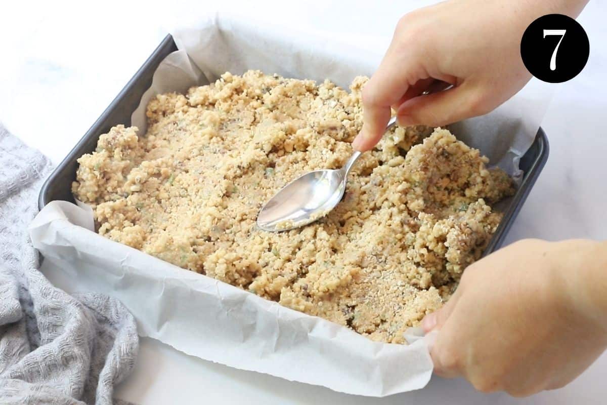 a hand with a spoon, pressing slice mixture into a tin.