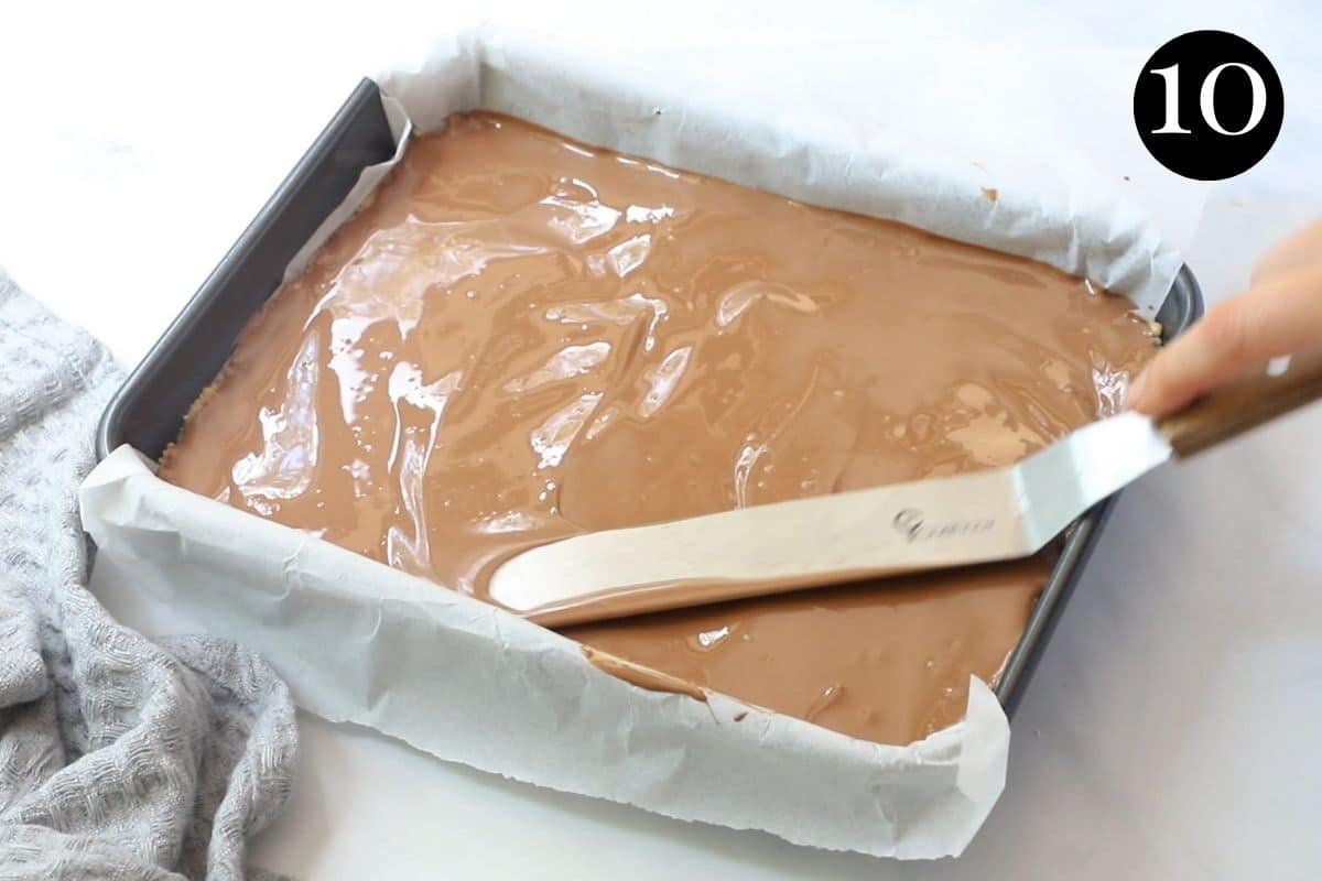 melted chocolate being spread over biscuit base with a spatula.