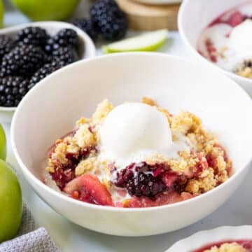 apple and blackberry crumble in a white bowl topped with ice cream.