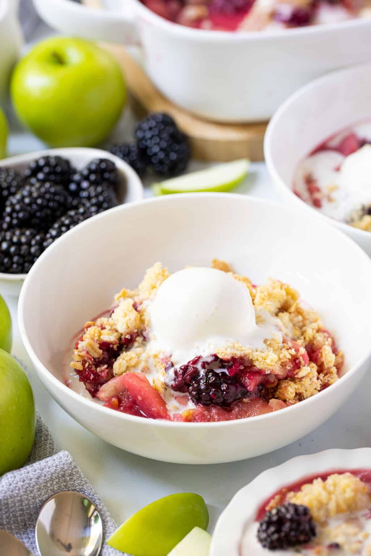 apple and blackberry crumble in a white bowl, topped with ice cream.