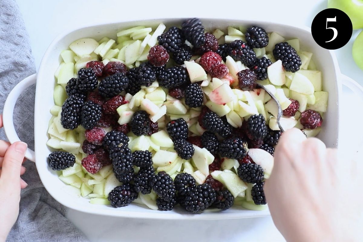 blackberries being folded into apple mixture in a baking dish.