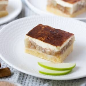 a piece of apple sour cream slice on a white plate with apple slices.